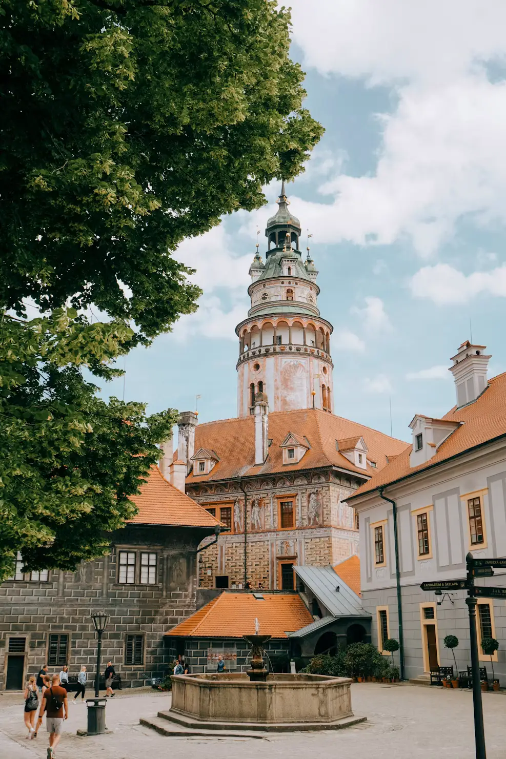 Cobblestone square with a fountain and a red-roofed clock tower in Český Krumlov.
