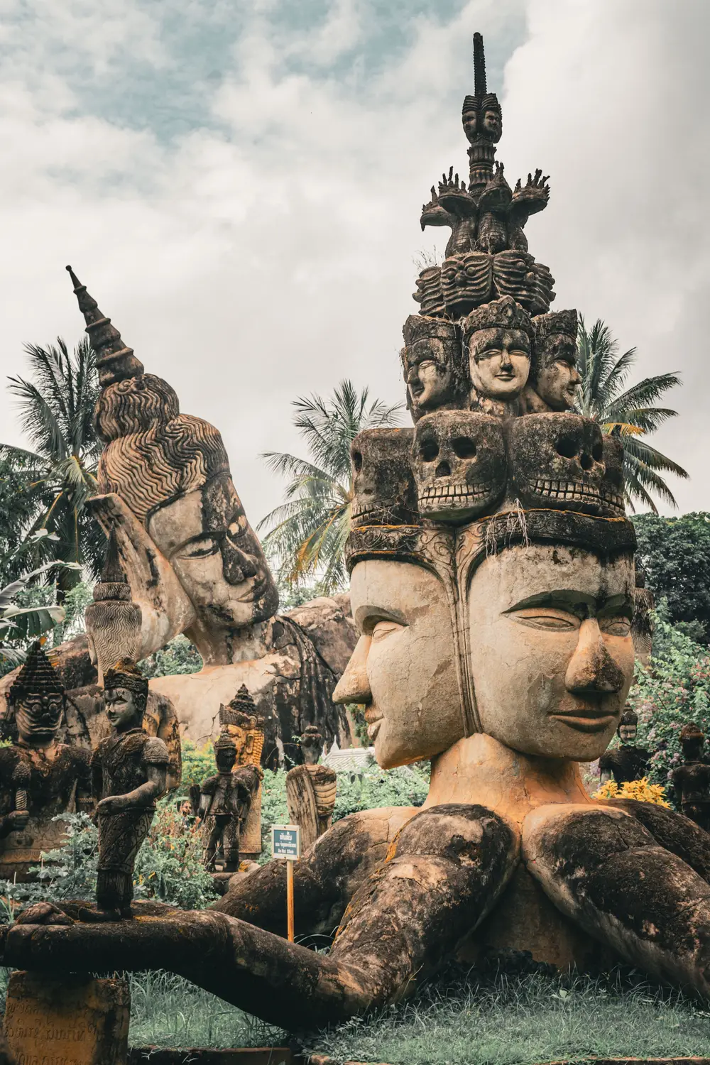 Weathered religious stone sculptures with multiple faces and skulls among palm trees at Buddha Park (Xieng Khuan) near Vientiane, Laos.Weathered religious stone sculptures with multiple faces and skulls among palm trees at Buddha Park (Xieng Khuan) near Vientiane, Laos.