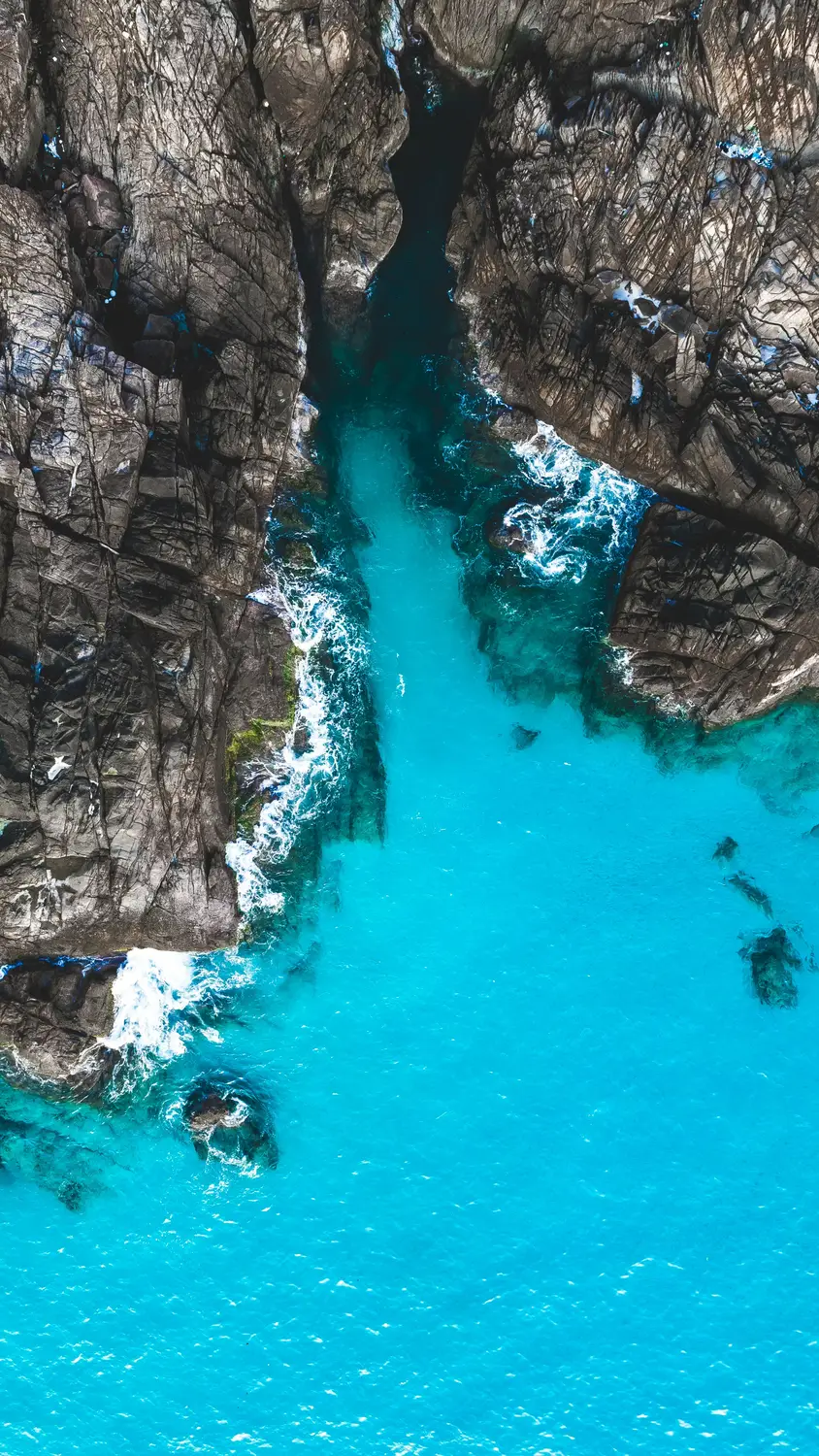 Aerial drone view of turquoise blue ocean water flowing through narrow rocky coastal cliffs in Malaysia