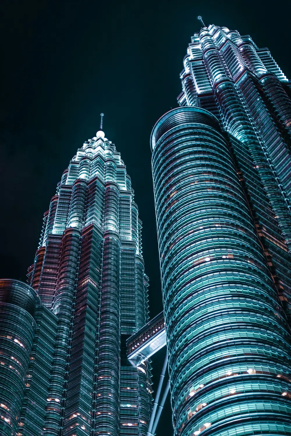 Low angle upward view of Petronas Twin Towers illuminated at night against dark sky in Kuala Lumpur Malaysia