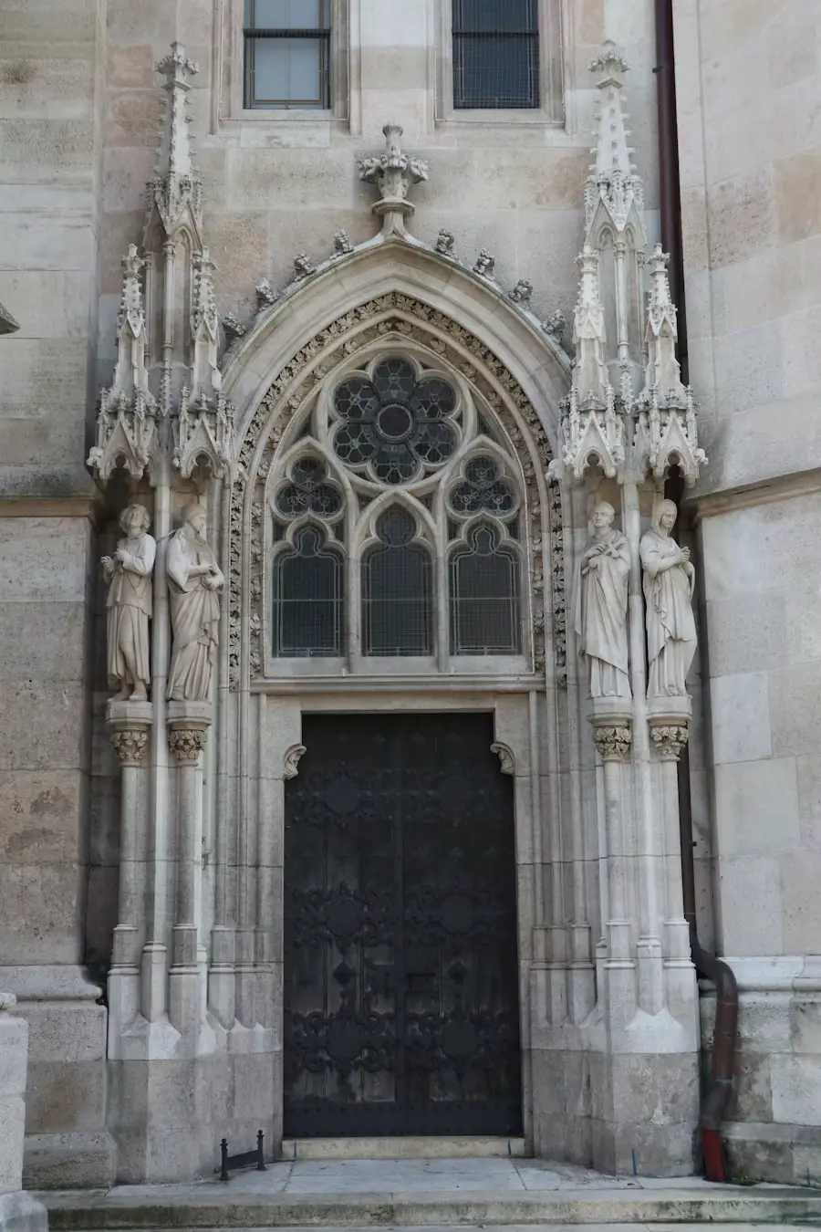 An ornate Gothic stone entrance with a large rose window and carved detailing above a dark wooden door.
