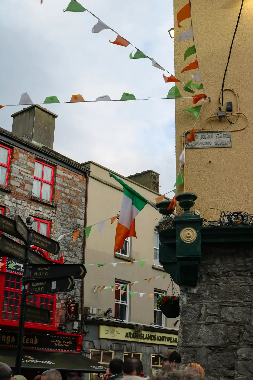 Colorful stone building with Irish flag bunting and red-framed windows along a street corner, Ireland.