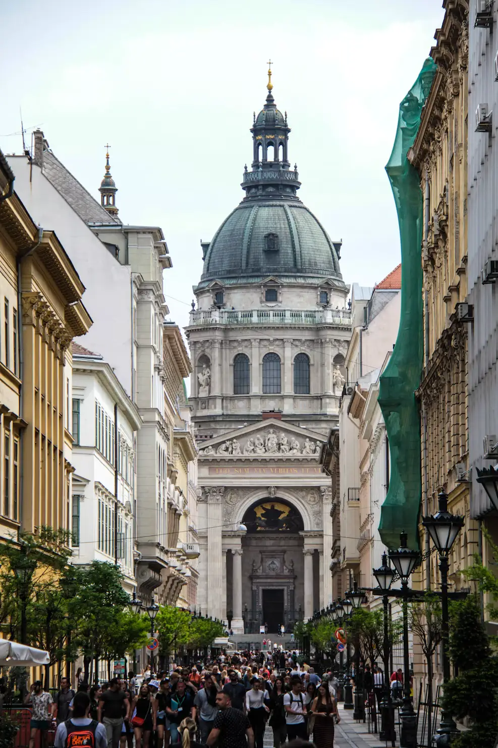 Grand domed basilica at the end of a busy tree-lined street filled with pedestrians.