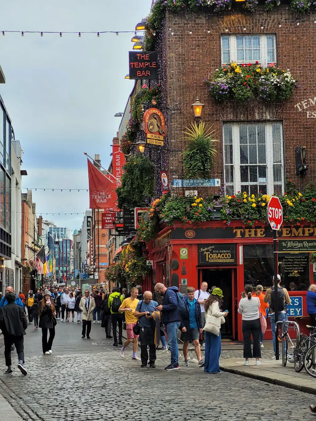 Crowded cobblestone street lined with colorful shopfronts and pubs, Ireland.