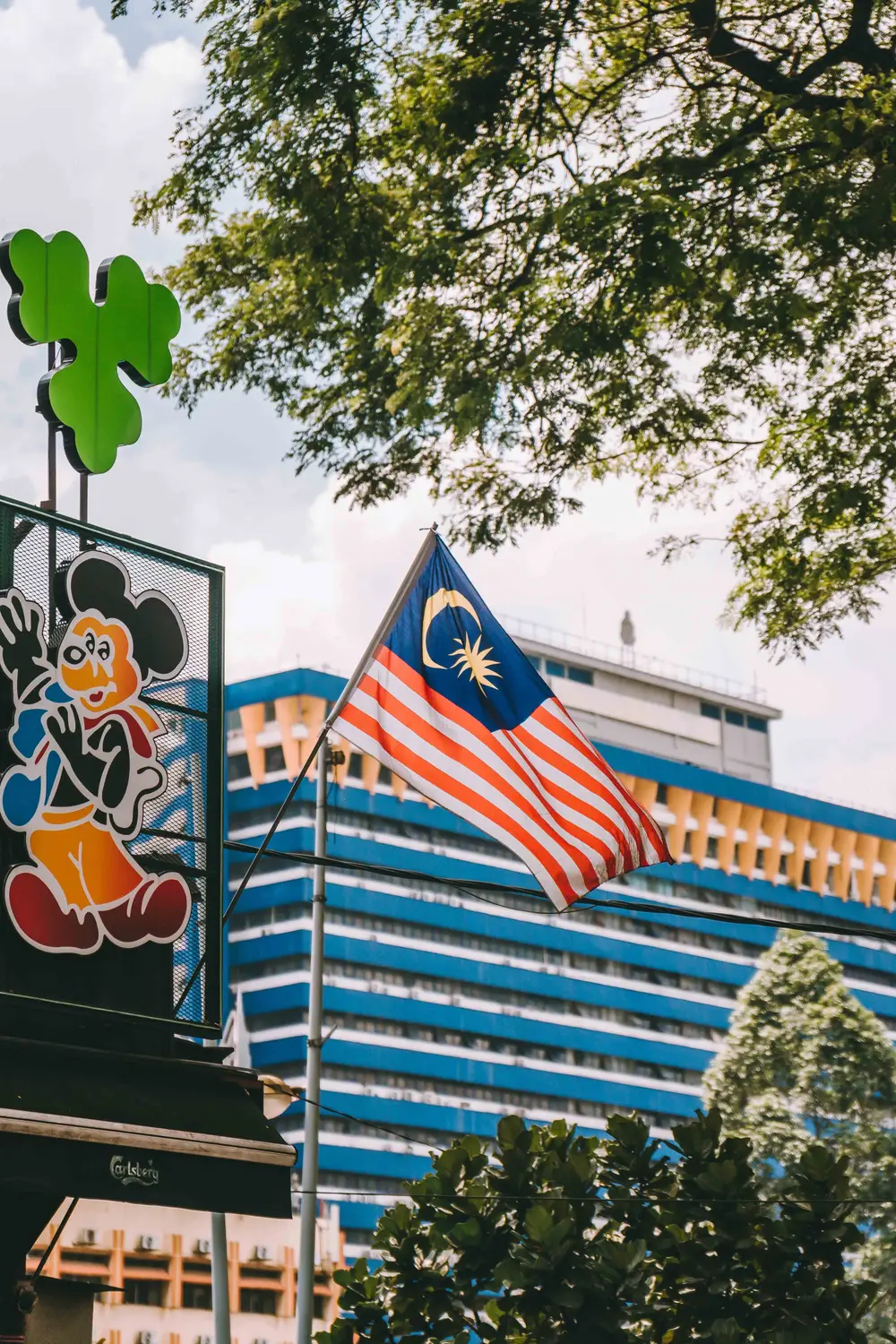 Malaysian Jalur Gemilang flag flying in front of modern blue glass office building with trees in Kuala Lumpur