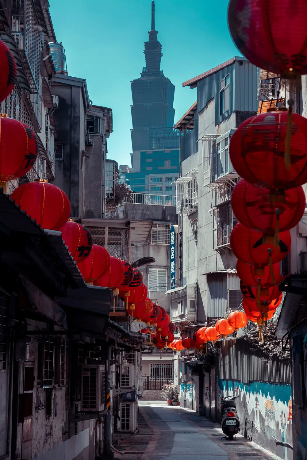 Red Chinese lanterns strung across a narrow Taipei alley with Taipei 101 tower rising in the background