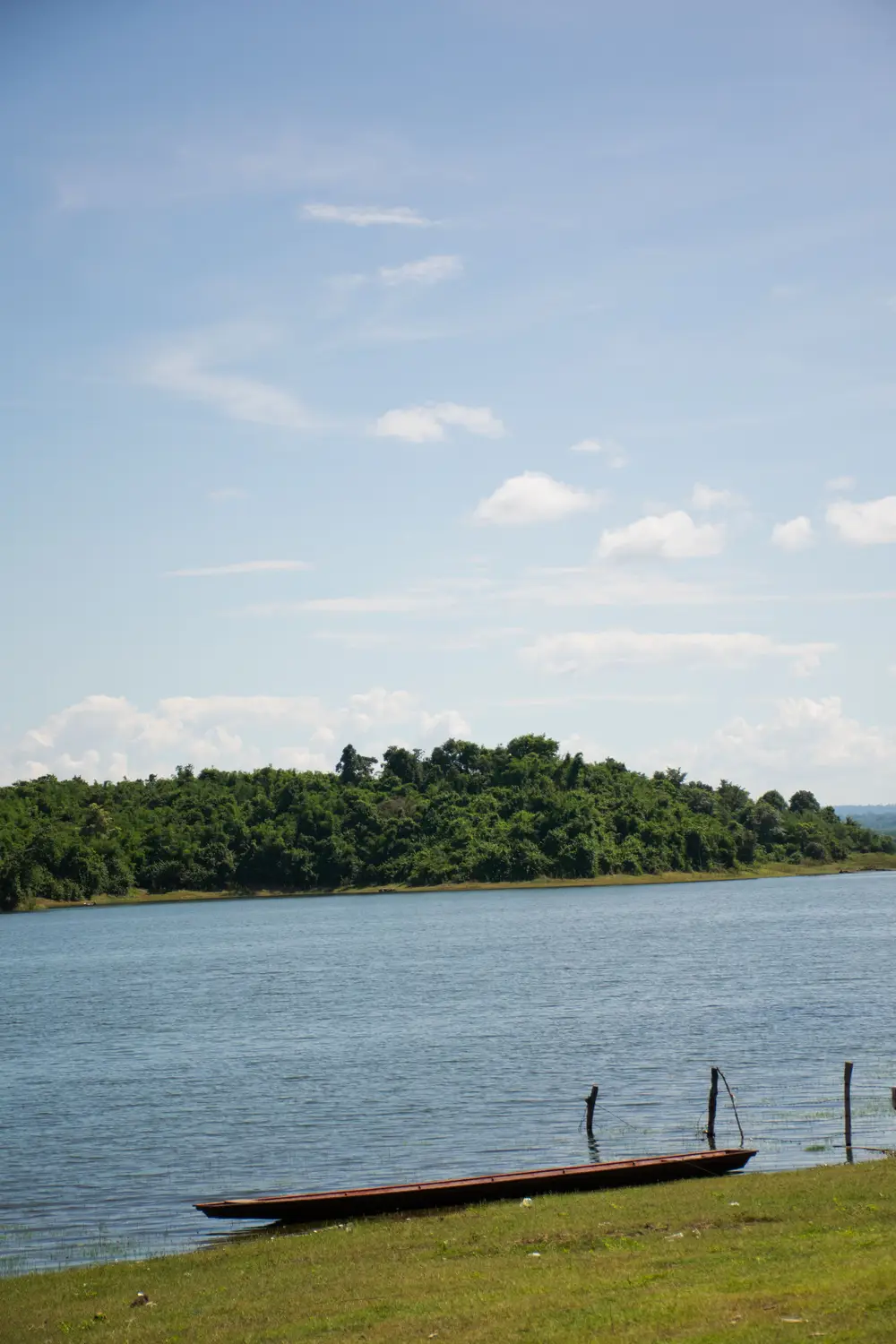 Wooden boat moored on the calm Mekong River beneath a blue sky with forested banks in Laos.