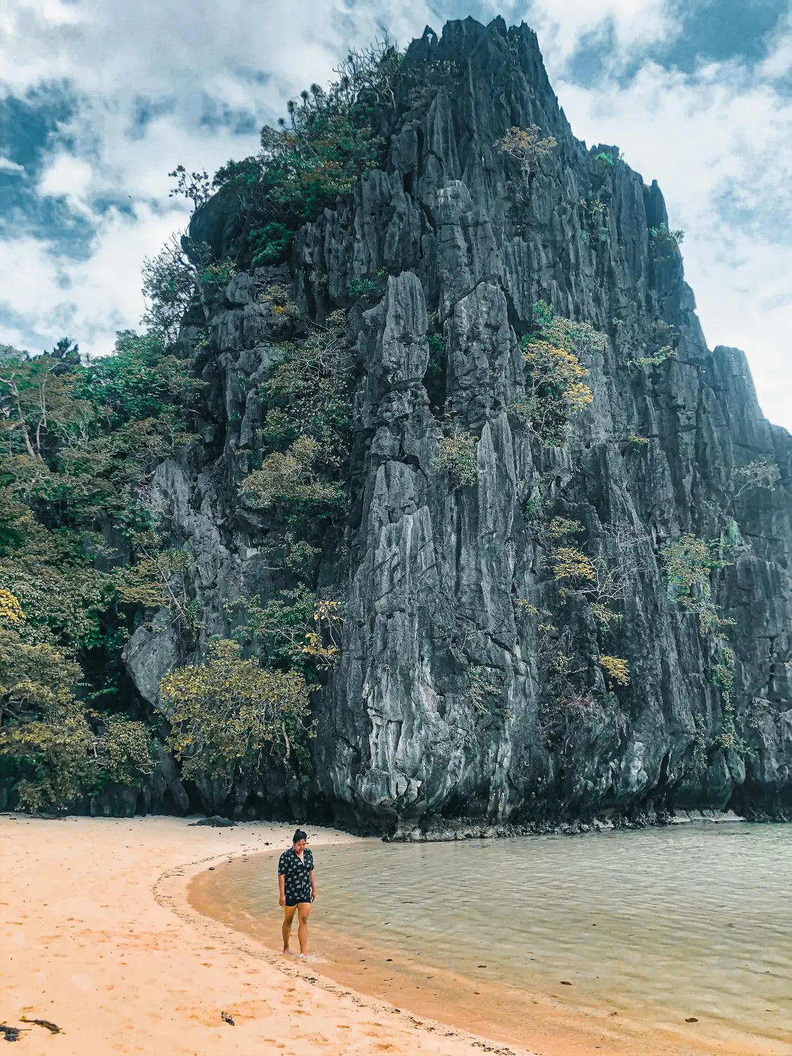 Person walking on a sandy beach beneath towering limestone karst cliffs in El Nido, Palawan, Philippines.