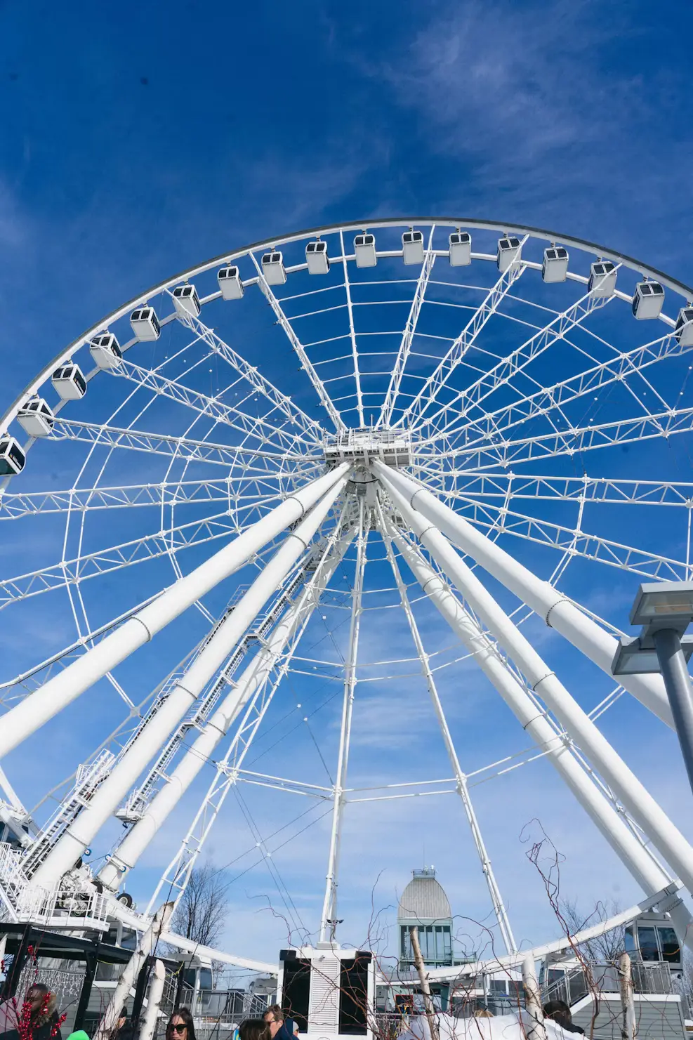 A large white Ferris wheel against a bright blue sky, with people gathered below.