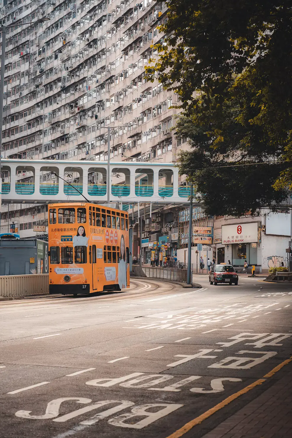 Vintage orange double-decker tram on a quiet street lined with dense residential buildings in Hong Kong.