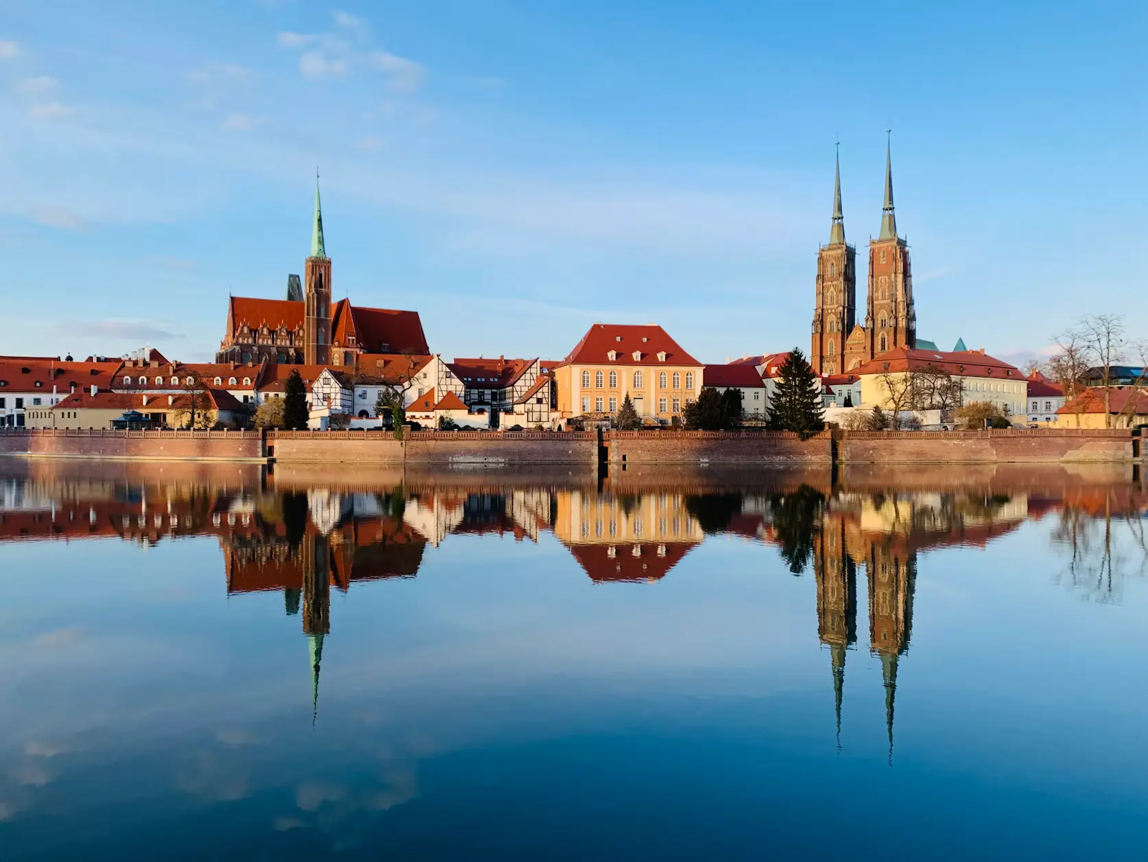 Historic Polish city skyline with church spires and traditional buildings reflected in calm water.