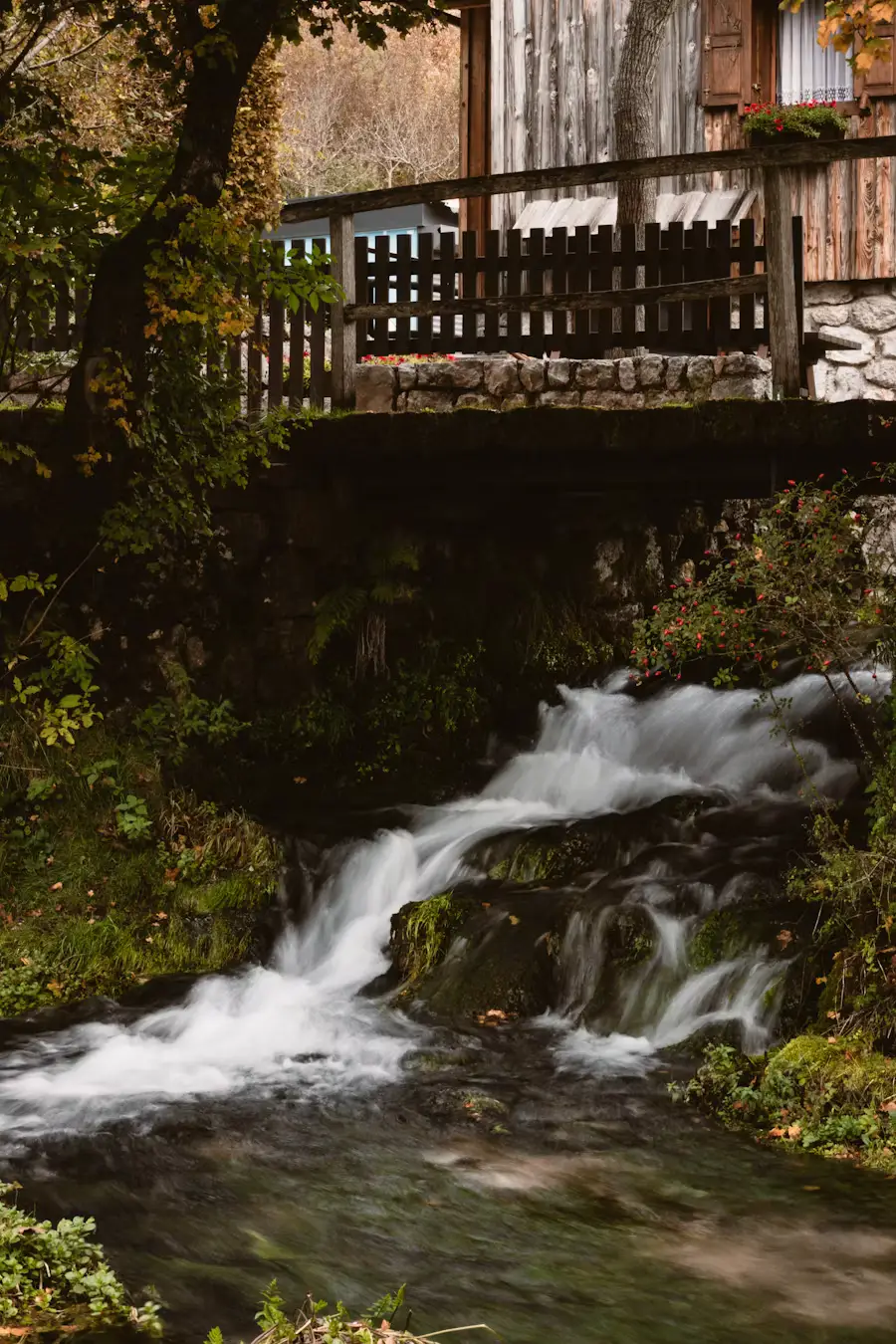 Small wooden mill house perched over a rocky stream with cascading water below.