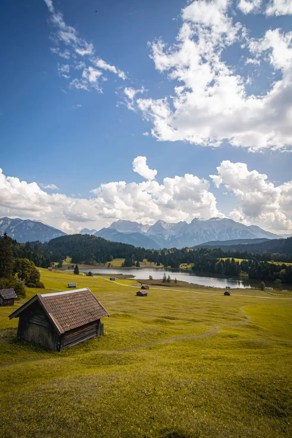 Green Alpine meadow with a wooden hut, lake, and mountain range in the distance