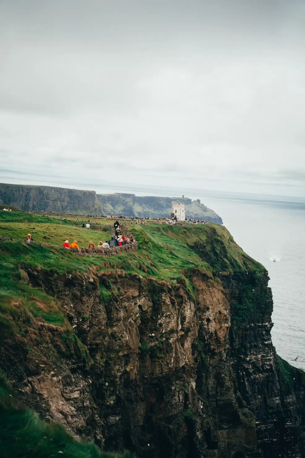 Dramatic sea cliffs with green grass tops overlooking the ocean, people visible near the edge, Ireland.