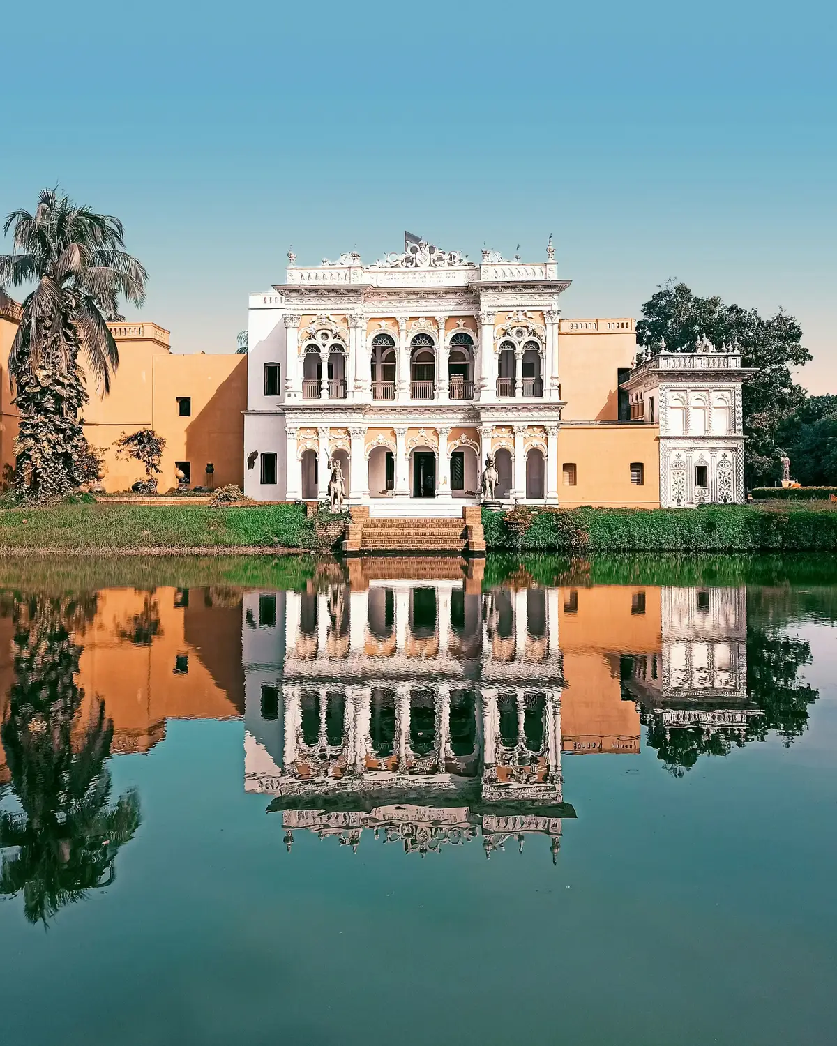 Ornate colonial-era Shoshi Lodge palace with Mughal-baroque architecture perfectly reflecting in a still pond, Mymensingh, Bangladesh
