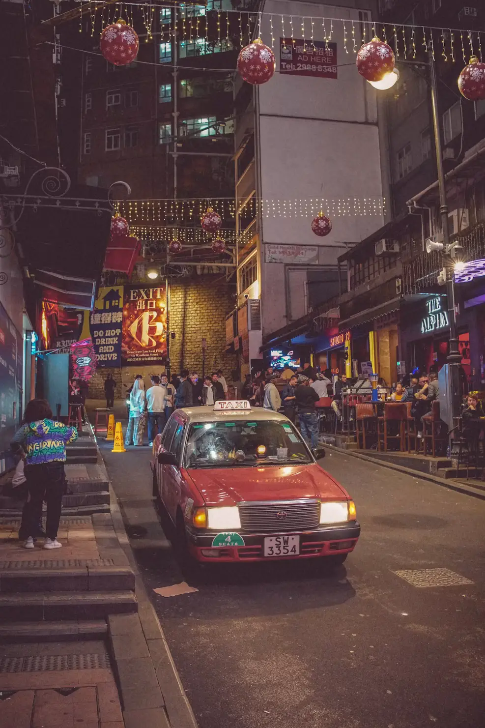 Red taxi driving down a busy neon-lit street lined with shops and signs in Hong Kong.
