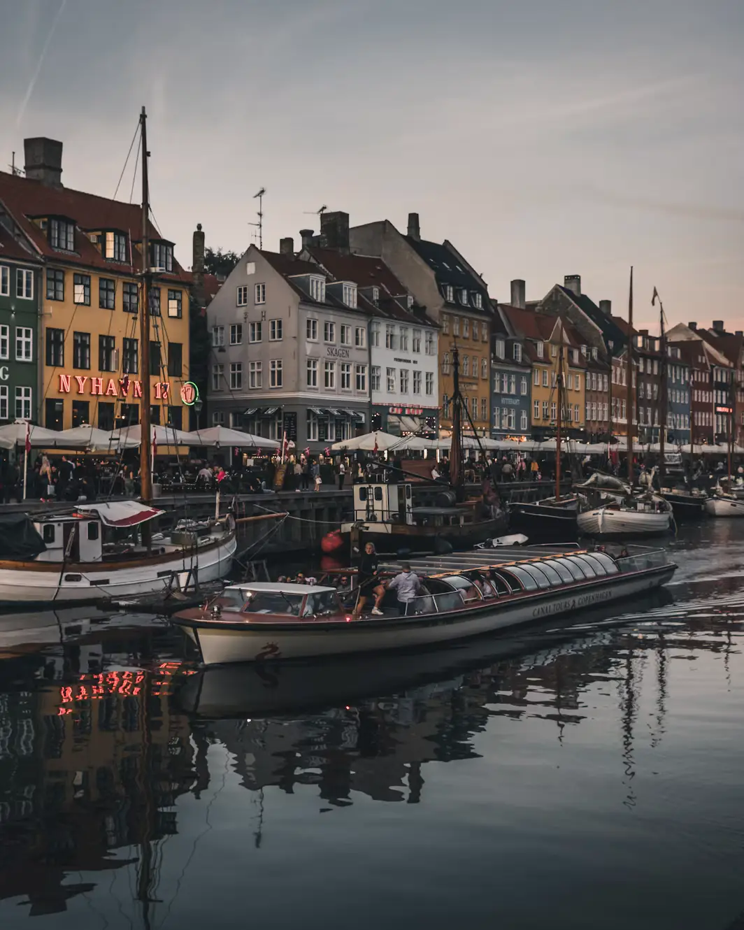Nyhavn canal at dusk with moored boats reflecting in the water beside colorful houses