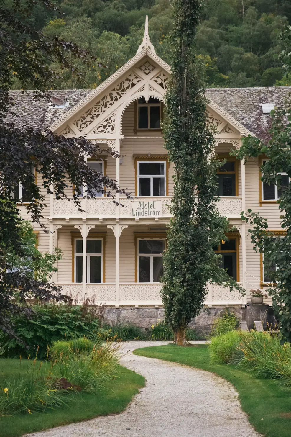 A gravel path leading to a historic white wooden hotel with ornate gables, framed by lush gardens.