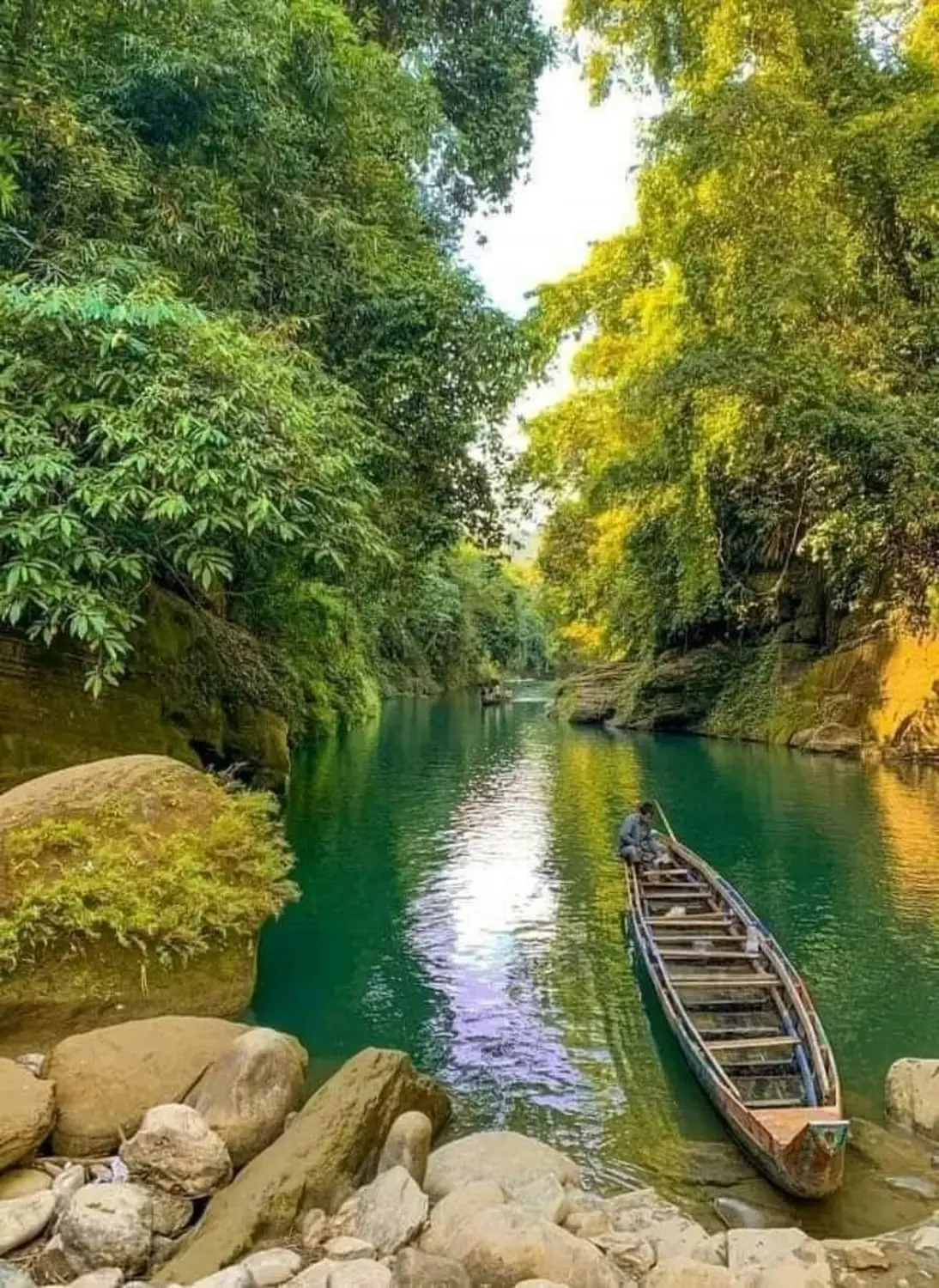 Wooden boat on crystal-clear turquoise river gorge surrounded by lush green jungle, Shari Goyain River, Sylhet, Bangladesh