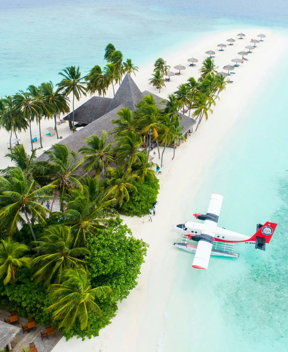 TMA seaplane landed on white sand beach beside tropical island resort with palm trees and beach umbrellas in the Maldives