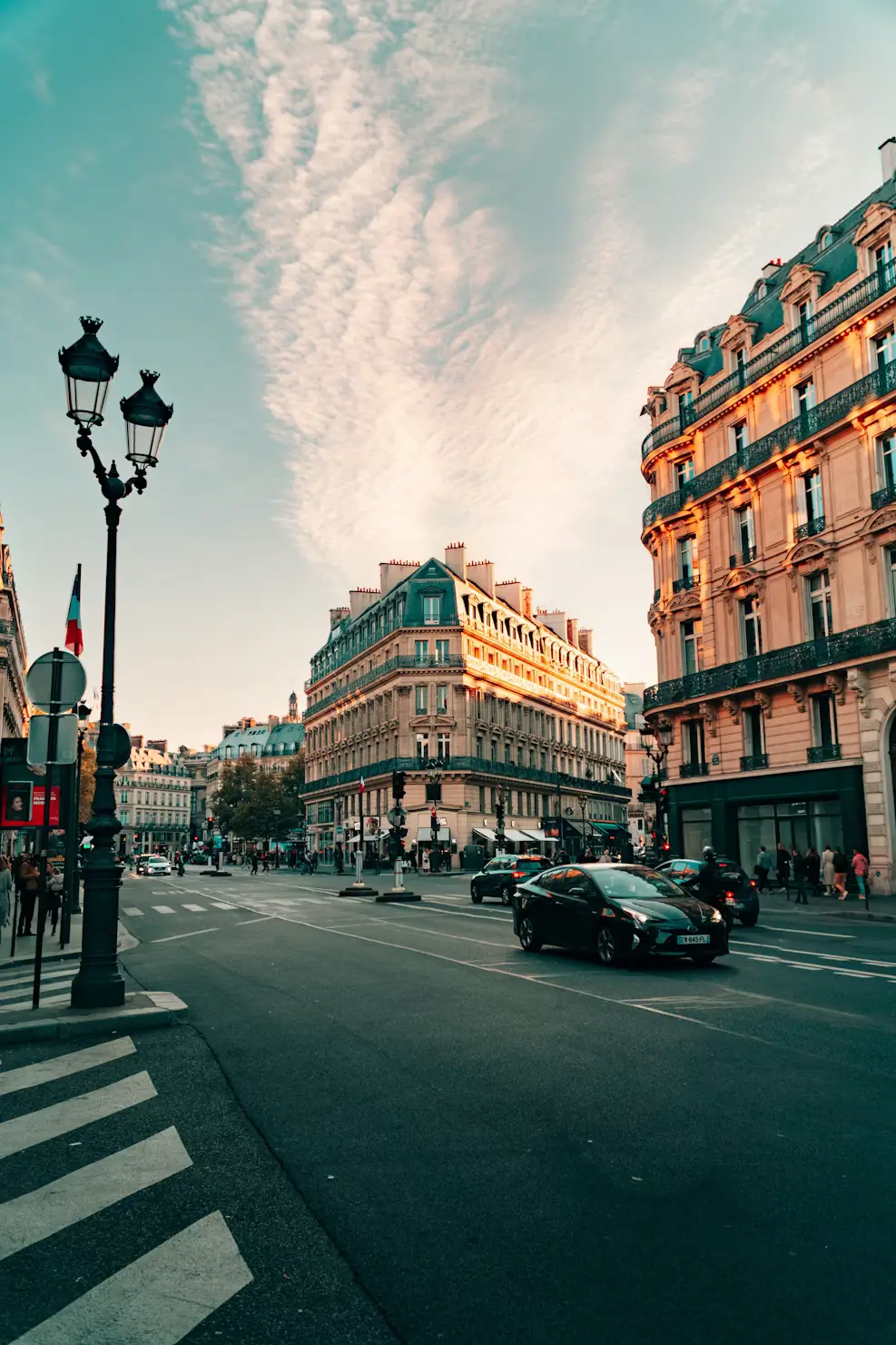 Parisian street at dusk with a wrought-iron lamppost and vintage cars