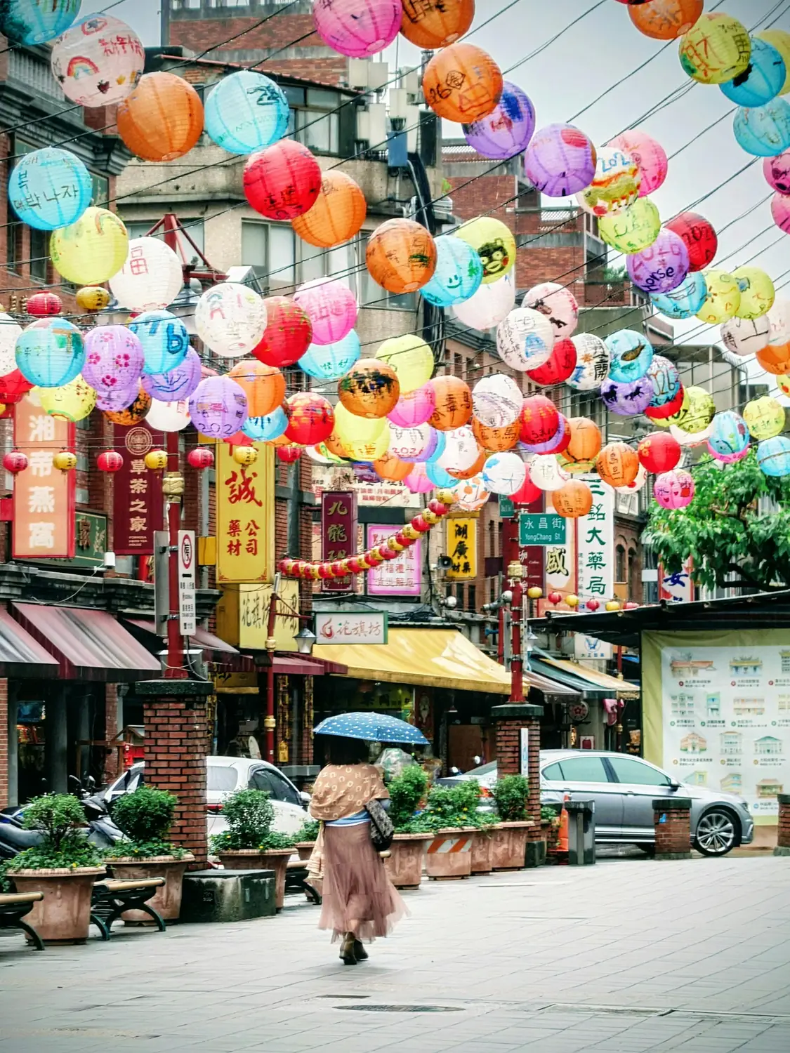 Woman with a blue umbrella walking down a Taiwan street decorated with hundreds of colorful hand-painted paper lanterns