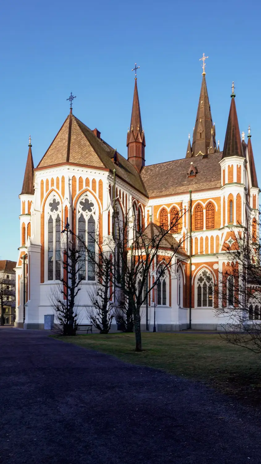 Gothic-style brick church with twin spires, seen from a park at dusk.