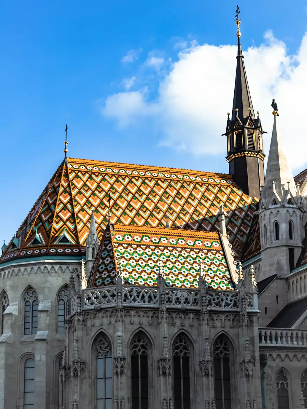 Patterned tiled roof with Gothic spires against a blue sky.