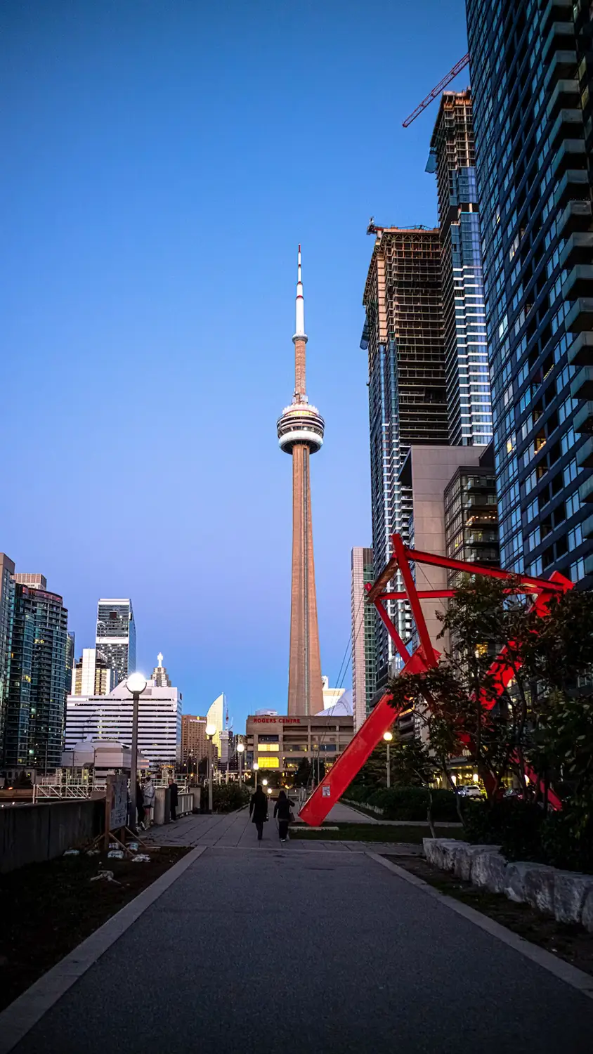 A nighttime view of Toronto's illuminated CN Tower and skyline along a walkway with red sculptural benches.