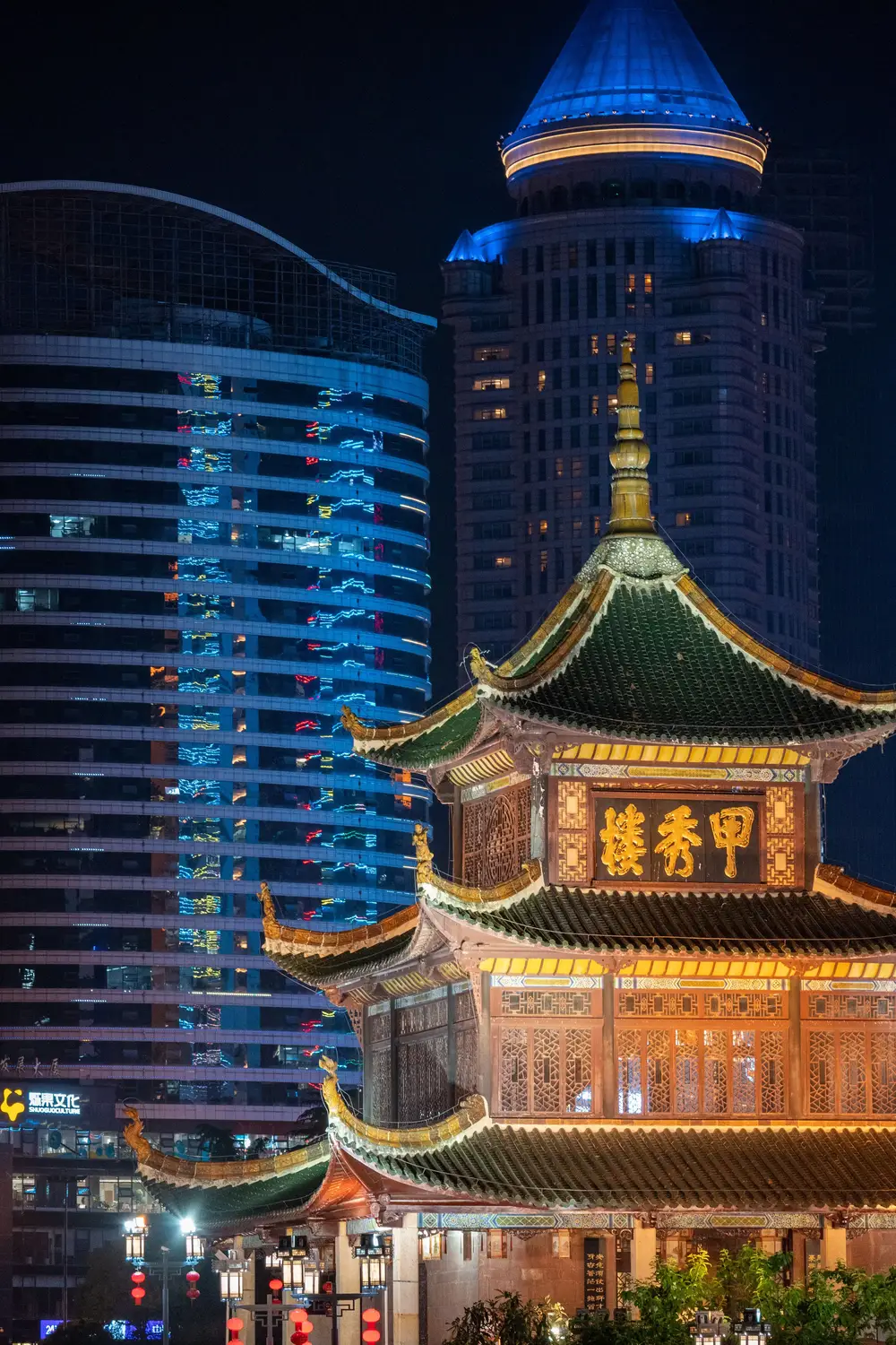 Jiaxiu Tower historic pavilion with green roof glowing at night against illuminated modern skyscrapers in Guiyang