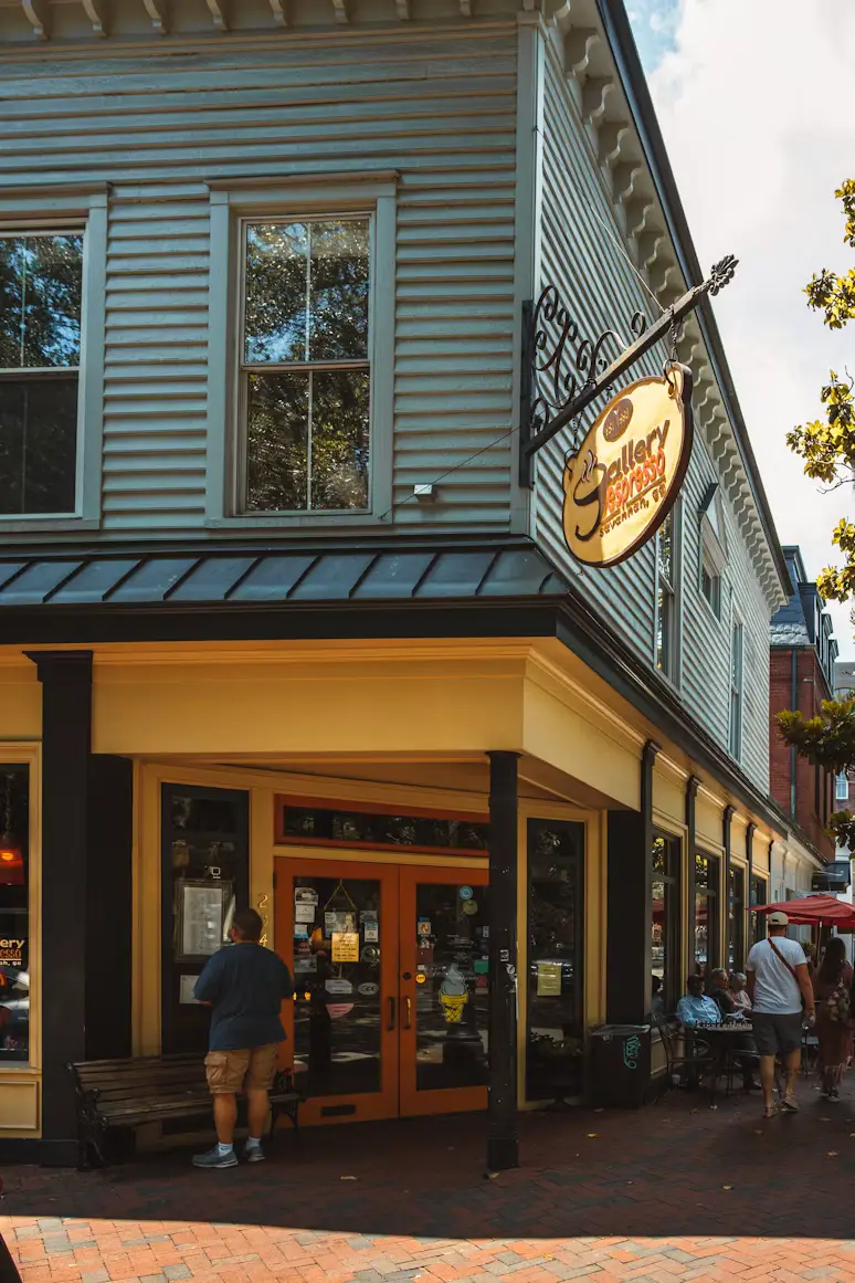 Corner restaurant entrance with a hanging sign and people walking along a brick sidewalk.