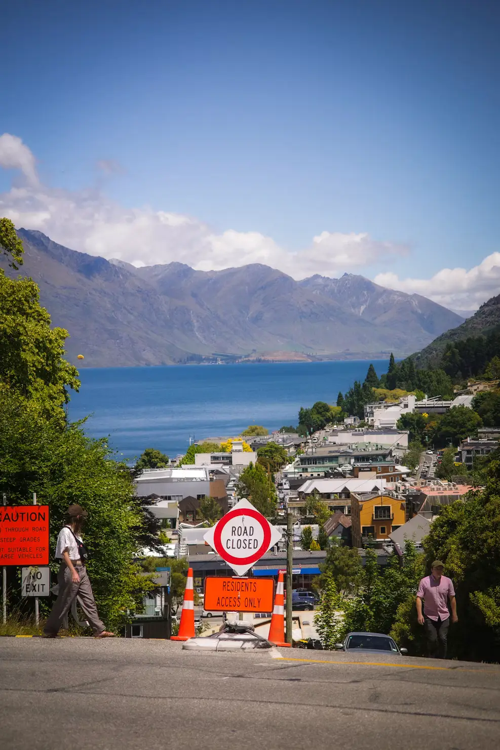 View over a lakeside town with mountains across the water and a road closure sign in the foreground.