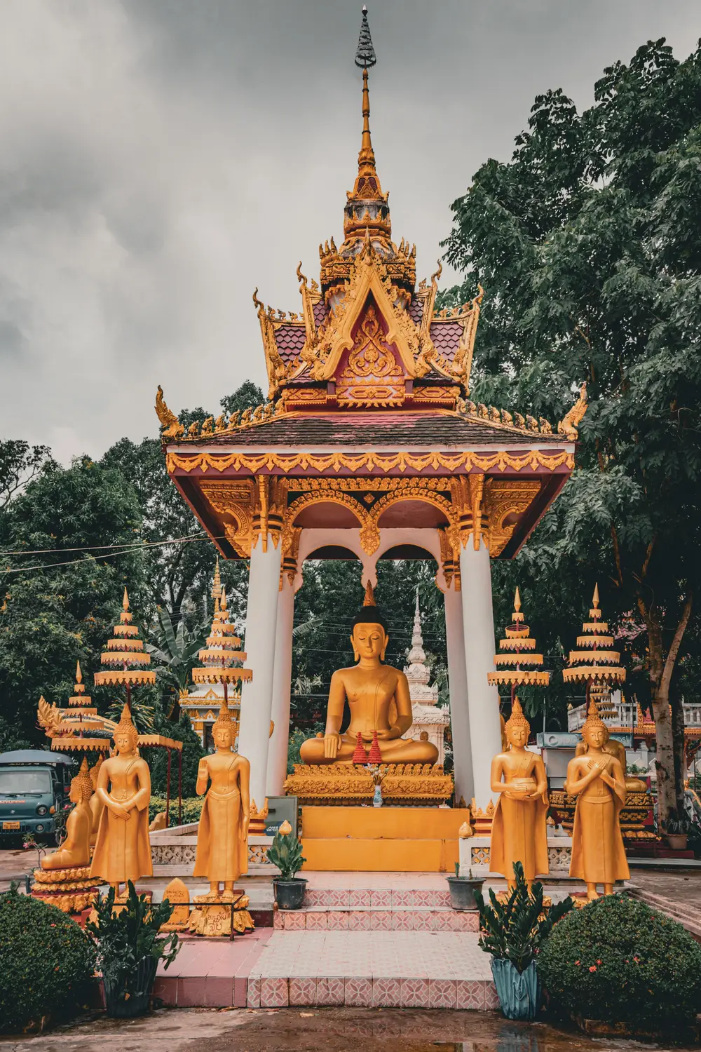 Ornate golden Buddhist temple shrine with a tiered spire under a cloudy sky in Laos.