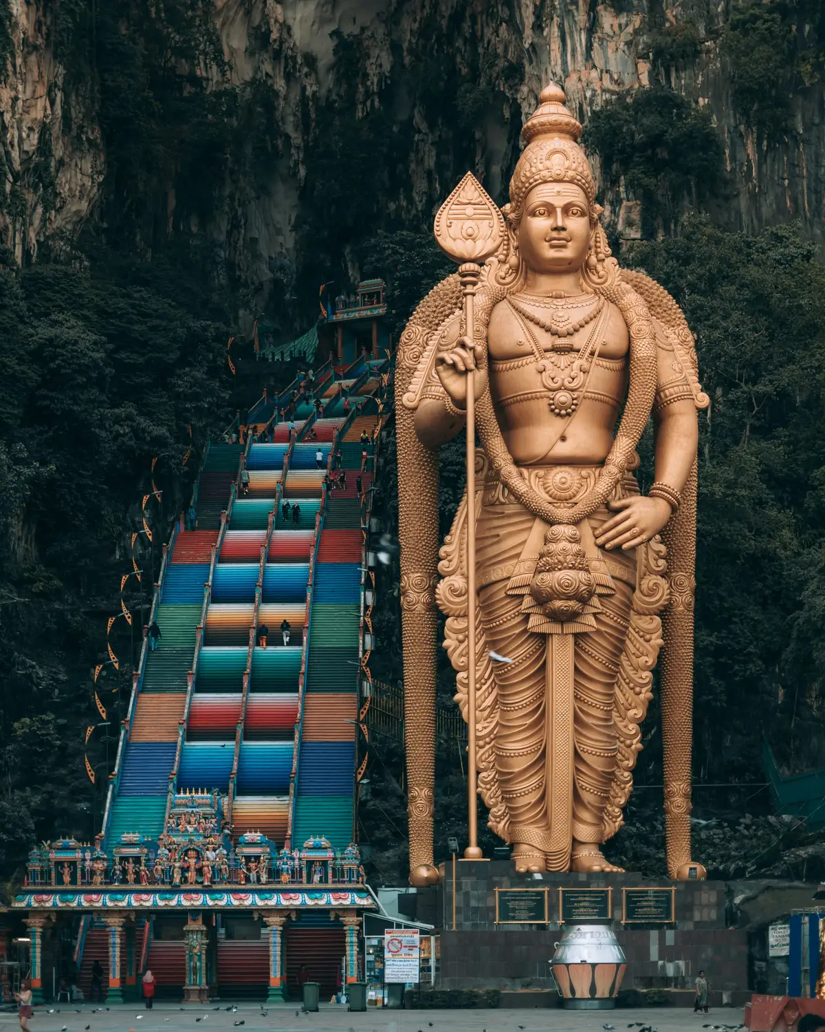 Giant golden Lord Murugan statue standing at entrance of Batu Caves Hindu temple with colorful stairs in Kuala Lumpur Malaysia