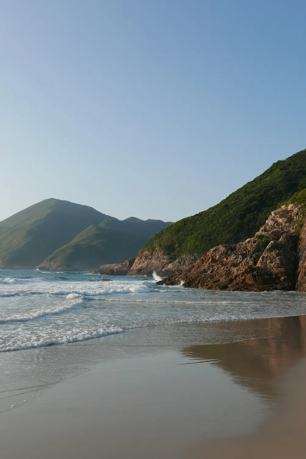 Secluded sandy beach with gentle waves and green forested headlands in Hong Kong.