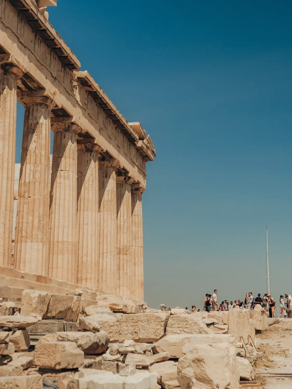 Tall marble columns of the Parthenon against a clear blue sky, with visitors exploring the ruins below.
