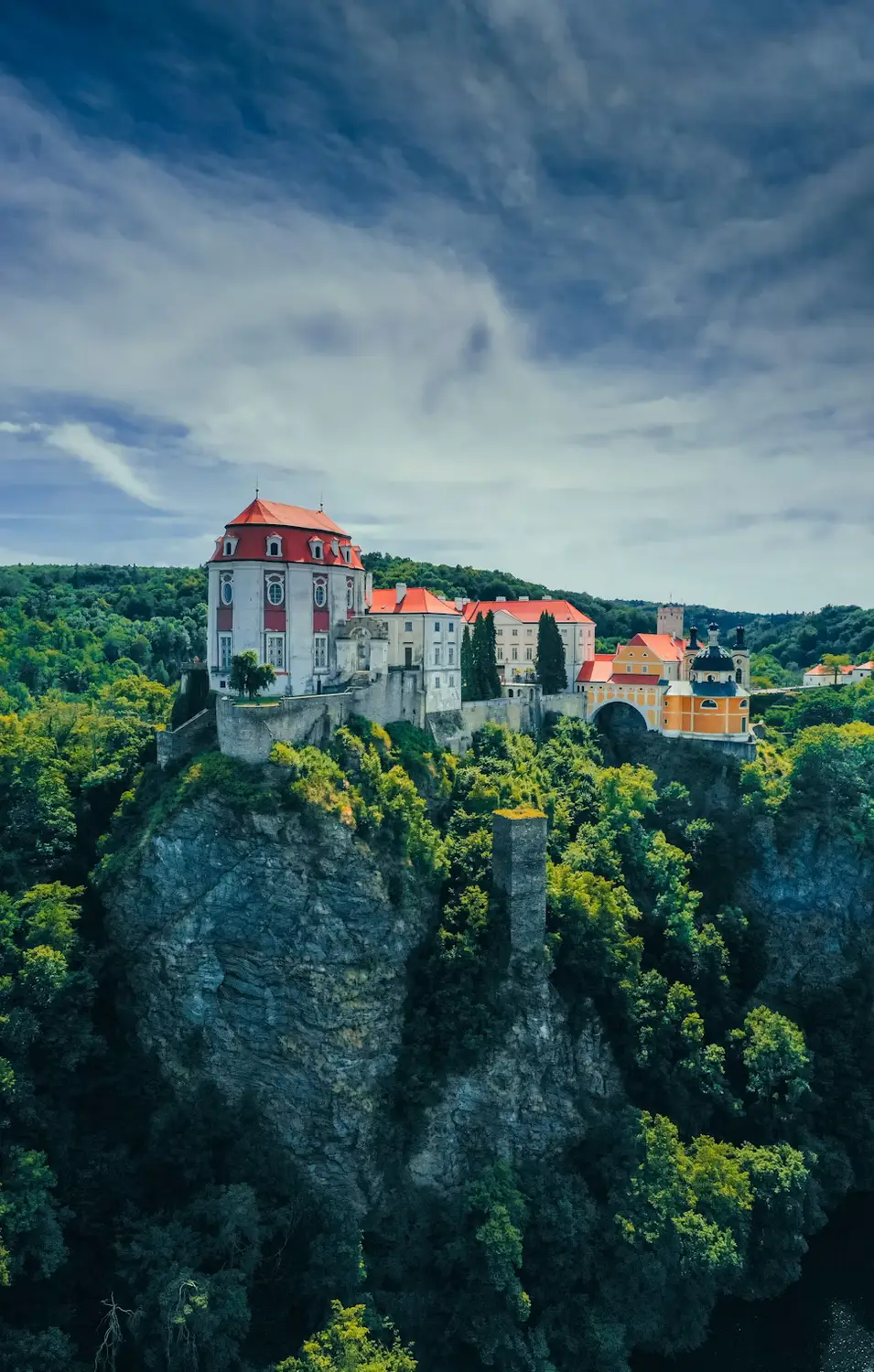 Castle perched atop a rocky sandstone outcrop surrounded by dense green forest under a cloudy sky.