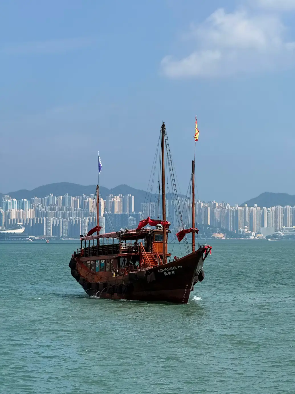 Traditional red-sailed Chinese junk boat sailing across Victoria Harbour with the skyline behind it in Hong Kong.