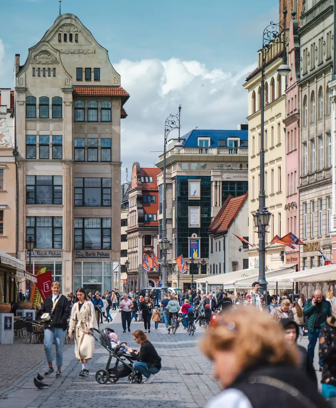 Busy European shopping street lined with historic buildings, cyclists, and pedestrians.