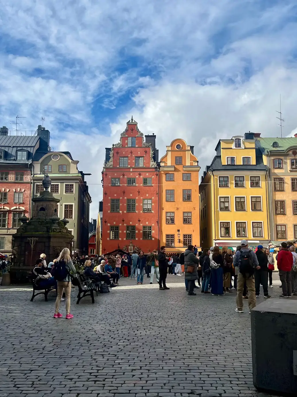 Colorful old town square lined with red, yellow, and orange buildings, filled with pedestrians.
