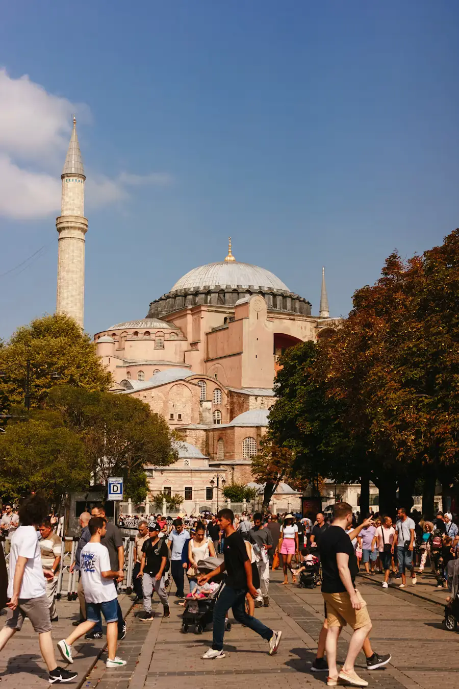 Crowds of people walking across the plaza in front of Hagia Sophia, with its dome and minaret rising above the trees.