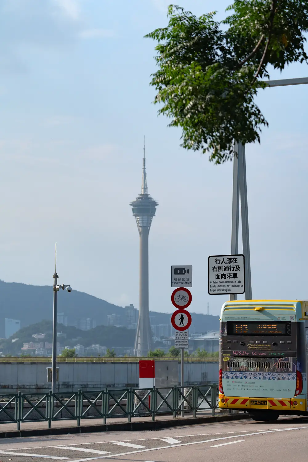 Street view of Macau Tower skyline with traffic sign and passing bus