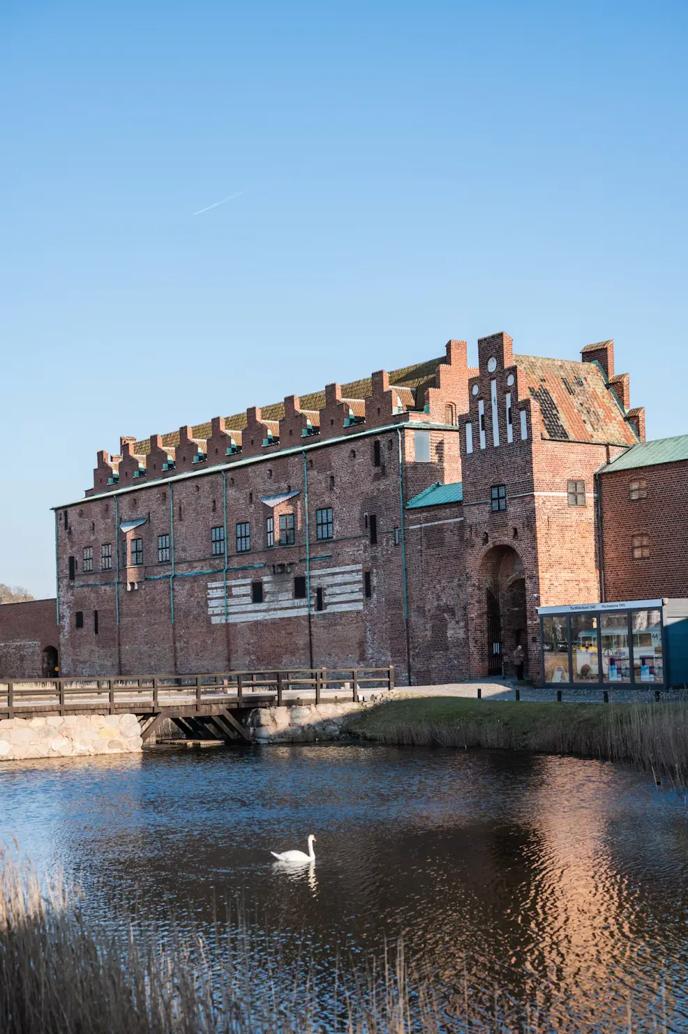 Brick building with a stepped gable beside a canal, with a swan floating on the water.