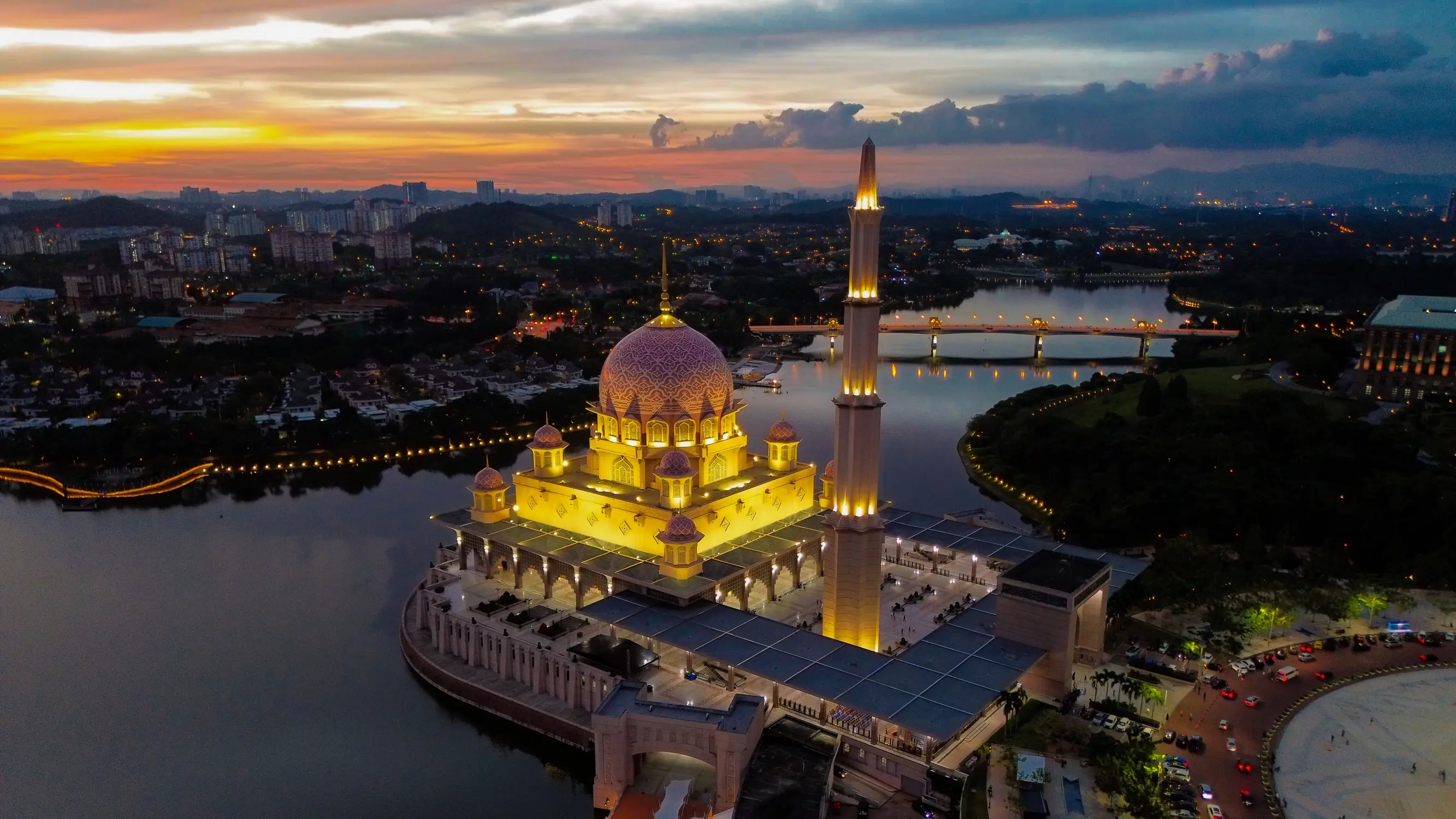 Aerial drone view of illuminated Putra Mosque at sunset in Putrajaya Malaysia with pink dome and city skyline