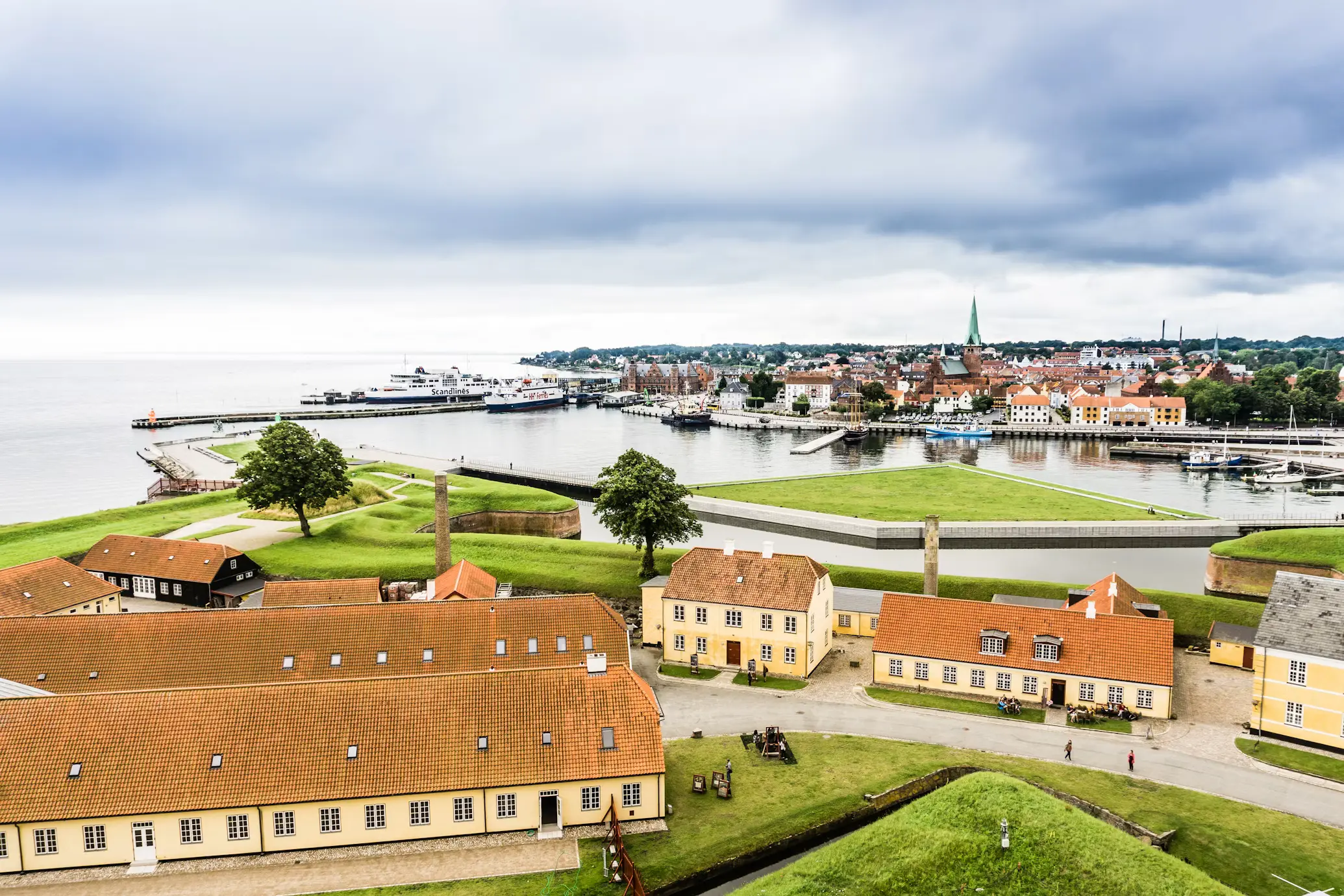 Aerial view of a Danish coastal town with red-roofed buildings, a marina, and the sea in the background