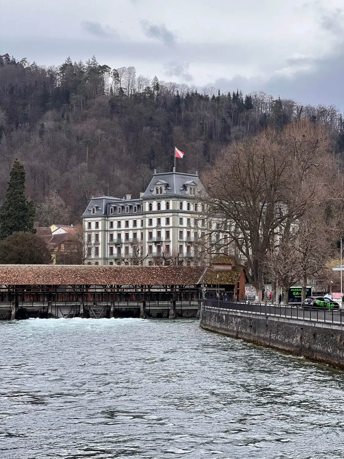 Historic covered wooden bridge over a river with a grand building beyond, Lucerne, Switzerland