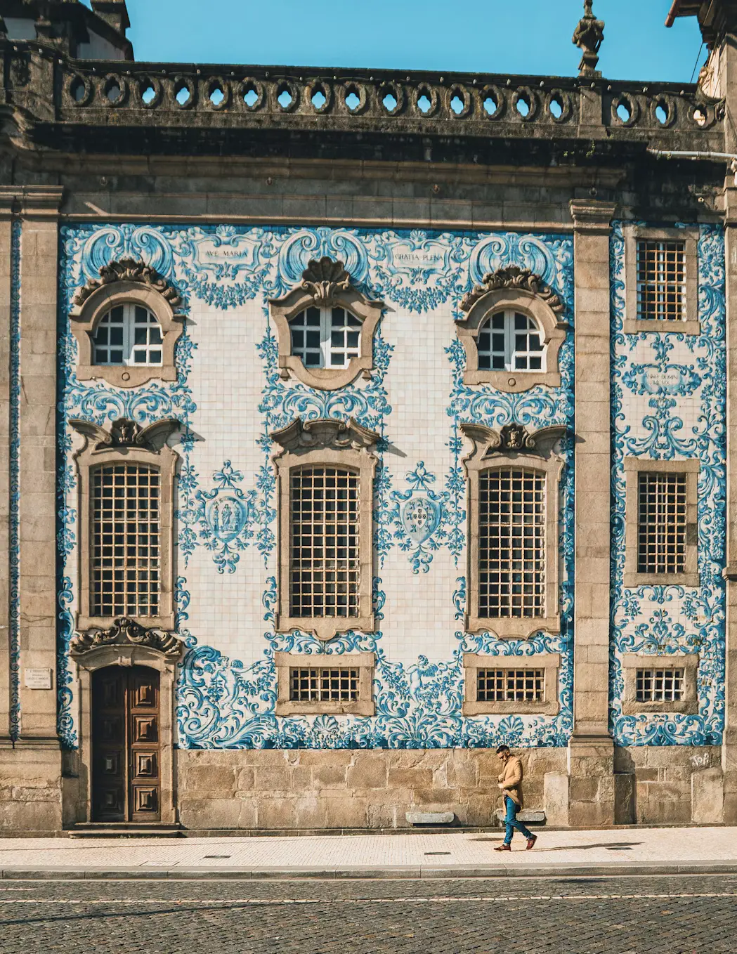Historic building facade covered in ornate blue-and-white ceramic tiles, with arched windows and a pedestrian walking along the street.