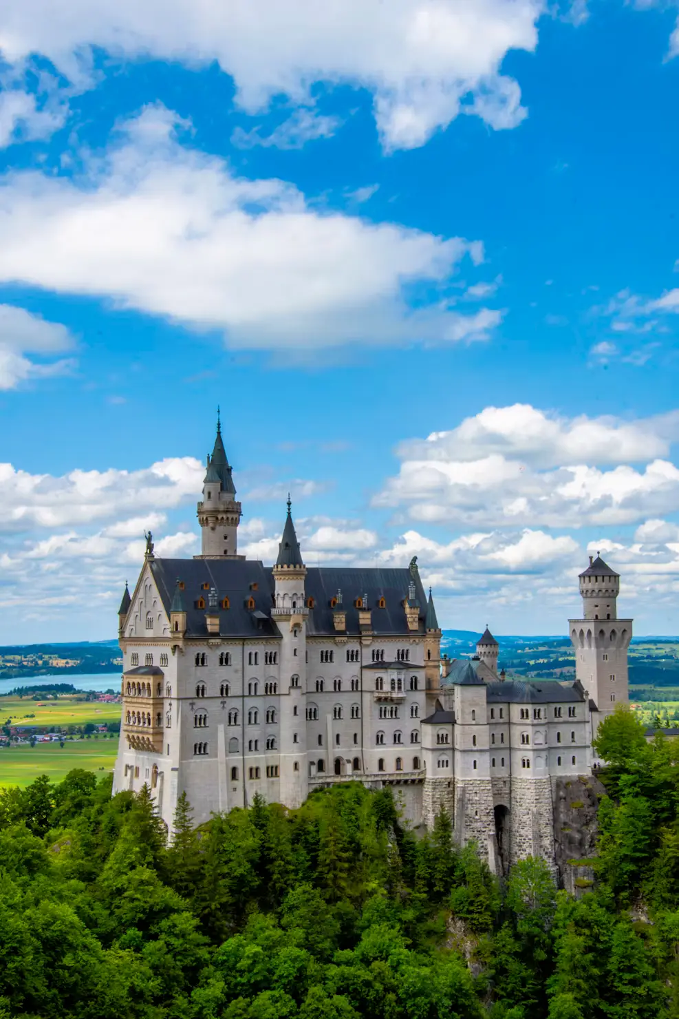 Neuschwanstein Castle surrounded by lush green forest under a blue sky with clouds