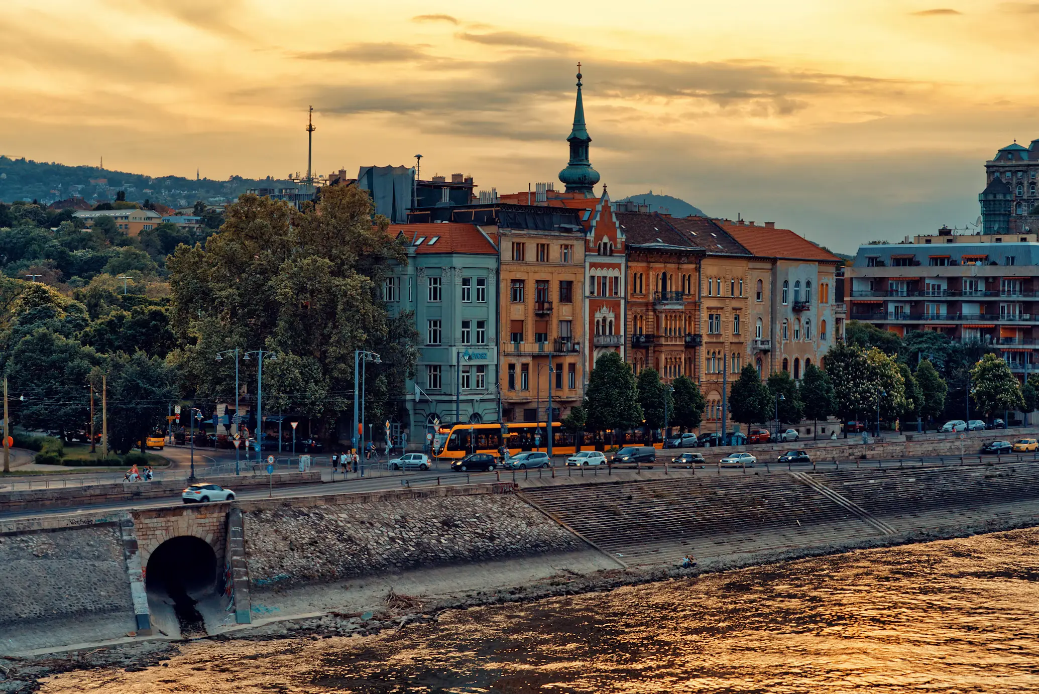 Historic riverside buildings and a church tower along the Danube at sunset.
