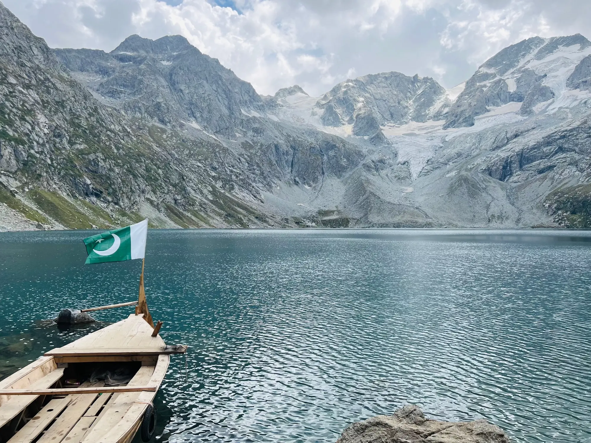 Wooden boat with Pakistan flag on Lulusar Lake with glacial mountain backdrop Kaghan Valley Pakistan